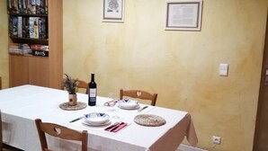 A dining area with a table set for four, wooden chairs, a wine bottle, and framed pictures on the wall. - Gîte in the heart of a vineyard. (Razac-de-Saussignac)