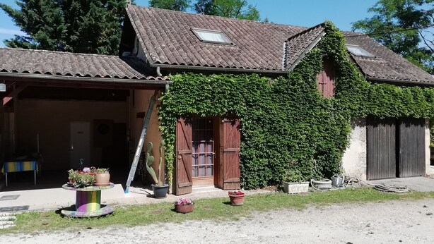 A building with a tiled roof, wooden doors, and a covered porch area with potted plants. - Gîte in the heart of a vineyard. (Razac-de-Saussignac)