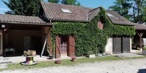 A building with a tiled roof, wooden doors, and a covered porch area with potted plants.