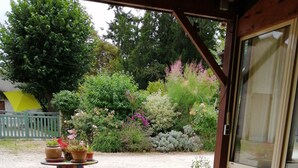 A round table with chairs, a bowl, a teapot, and a cup on a covered patio with a garden view. - Gîte in the heart of a vineyard. (Razac-de-Saussignac)