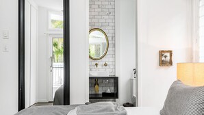 Un baño moderno con pared de azulejos blancos, un espejo redondo, un lavabo negro y un perchero para toallas.