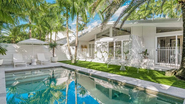Una casa moderna con piscina, un patio cubierto y un césped bien cuidado.