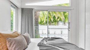 Un dormitorio con cama, almohadas y vistas a un balcón con plantas.