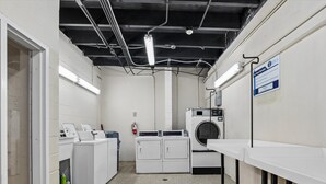 A laundry room with a washing machine, dryer, and stacked laundry baskets. - Sans Souci #605 | Gulf Front Condo! (Pensacola Beach)