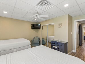 Habitación de hotel con dos camas, un escritorio, una silla, un televisor y un ventilador de techo.