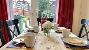 Une table à manger dressée avec des tasses blanches, des assiettes avec du pain et un vase rempli de fleurs blanches.