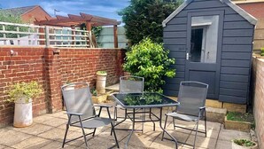 Une terrasse avec une table et quatre chaises, un petit abri de jardin et un mur en briques.