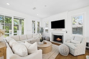 A modern living room with a sectional sofa, a round coffee table, a fireplace, and a flat-screen TV.