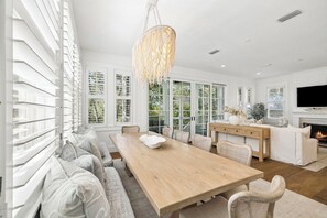 Un vaste espace dédié à la salle à manger, avec une longue table en bois, des sièges recouverts de tissu blanc et un lustre.