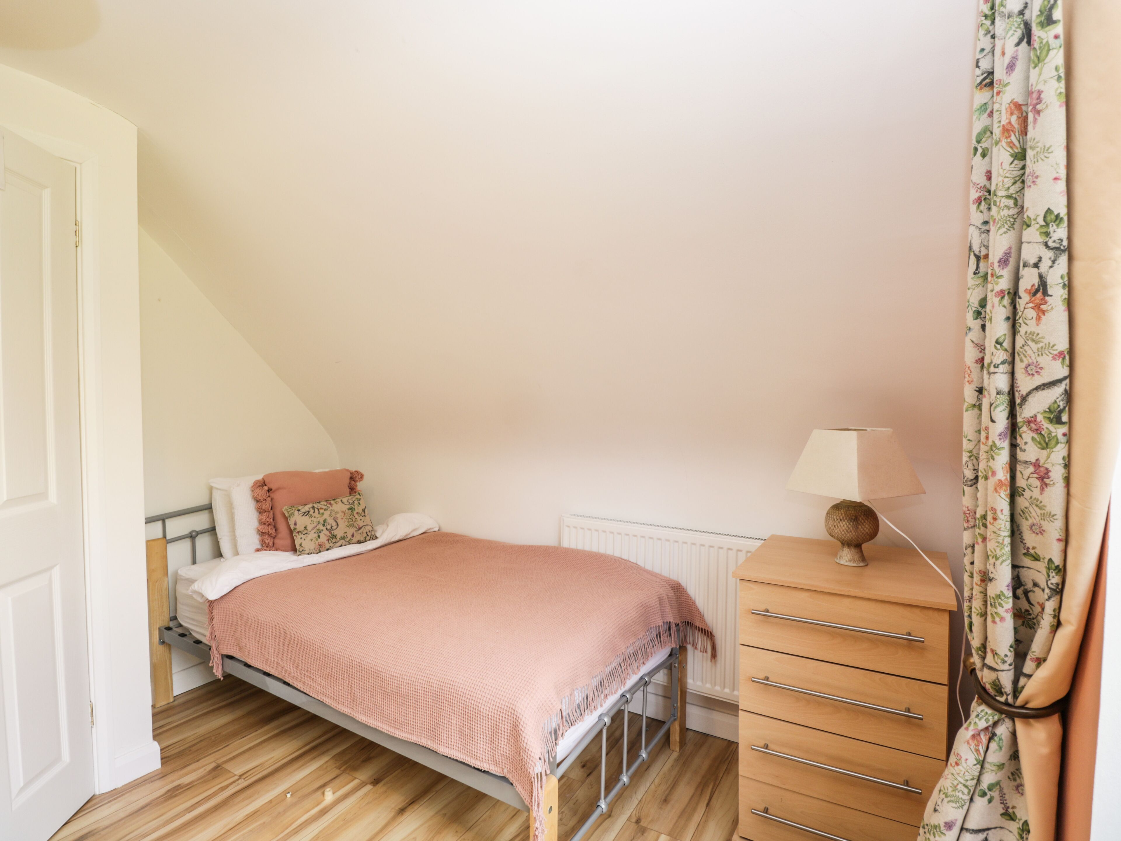 A bedroom with a bed, a dresser, a lamp, and a window with curtains.