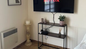 A room with a mounted TV displaying 'NETFLIX,' a framed abstract artwork, a small shelf with decorative items, and a radiator. - Charming country house with pool, ideal for vacations (Bannes)