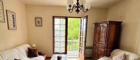 Un salon confortable avec un canapé, une table basse et un meuble. Une porte donne accès à un balcon d’où l’on peut admirer la verdure.