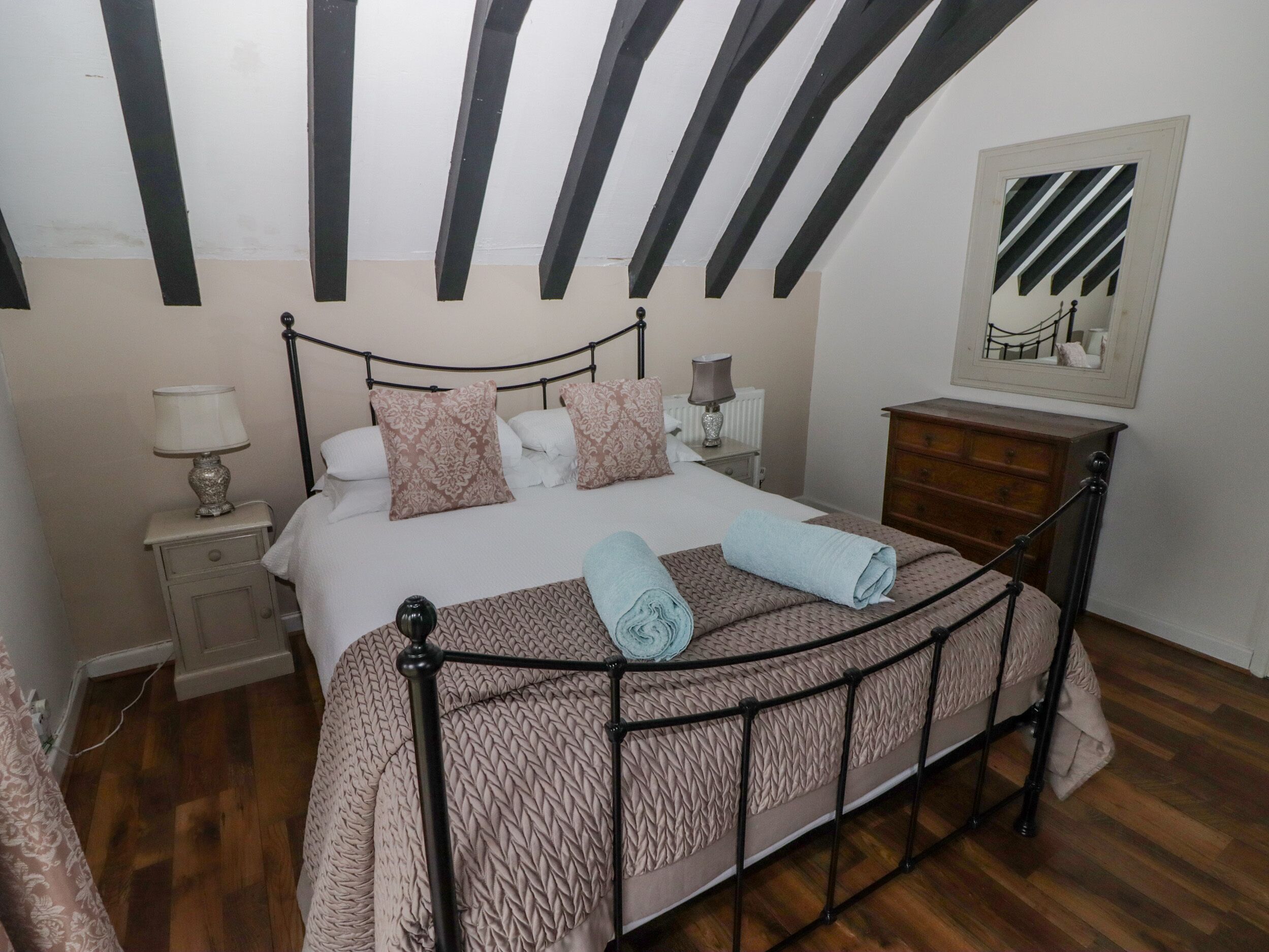 Un dormitorio con cama, mesitas de noche, cómoda y espejo en la pared.