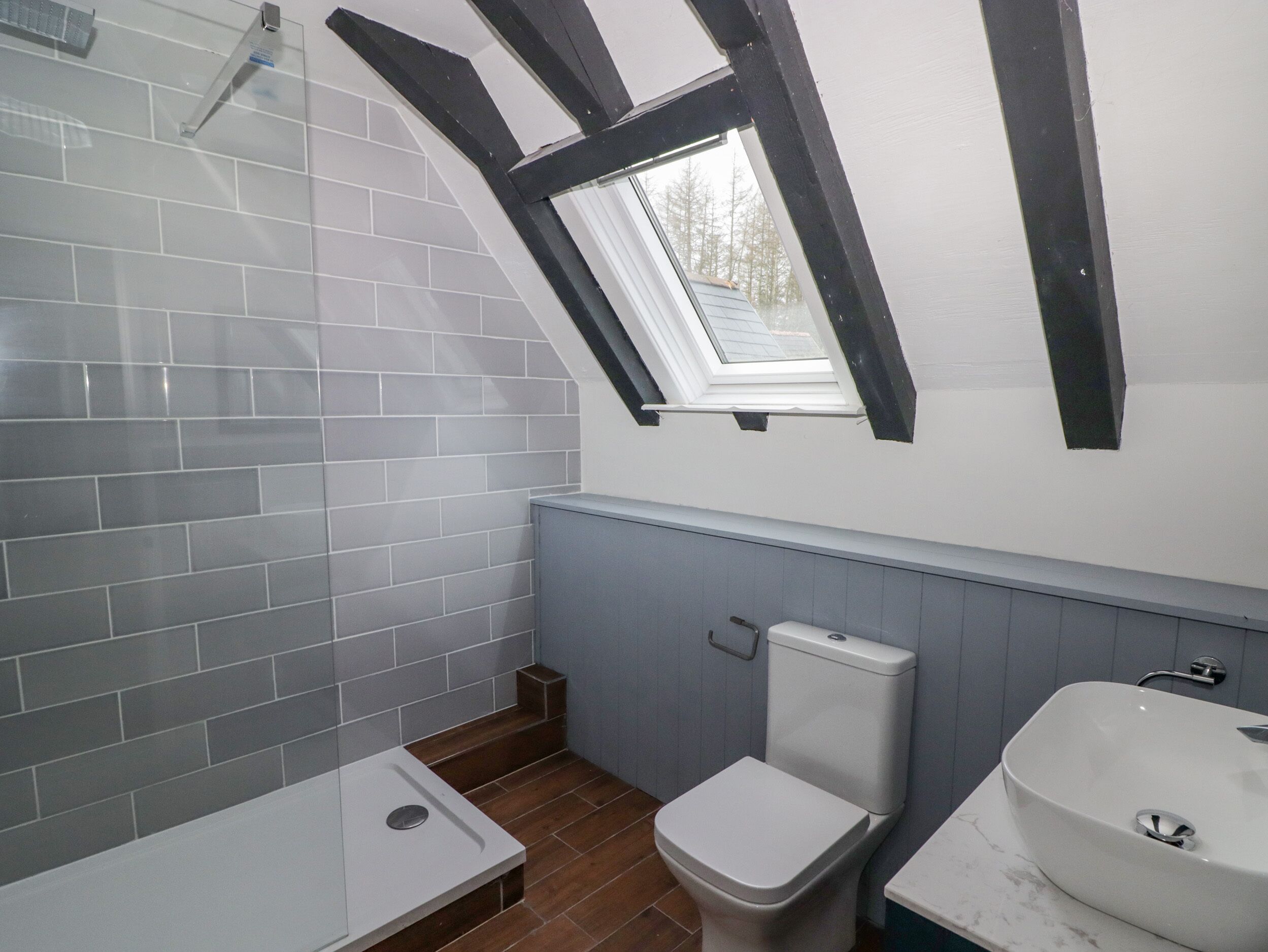 A bathroom with a skylight, white tiles, a toilet, and a sink.