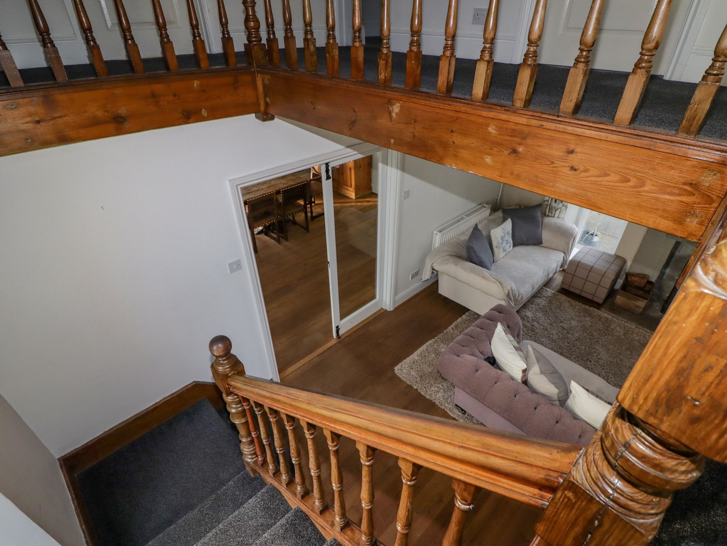 Een houten trap die leidt naar een slaapkamer op een entresol, met uitzicht op een woonkamer beneden.