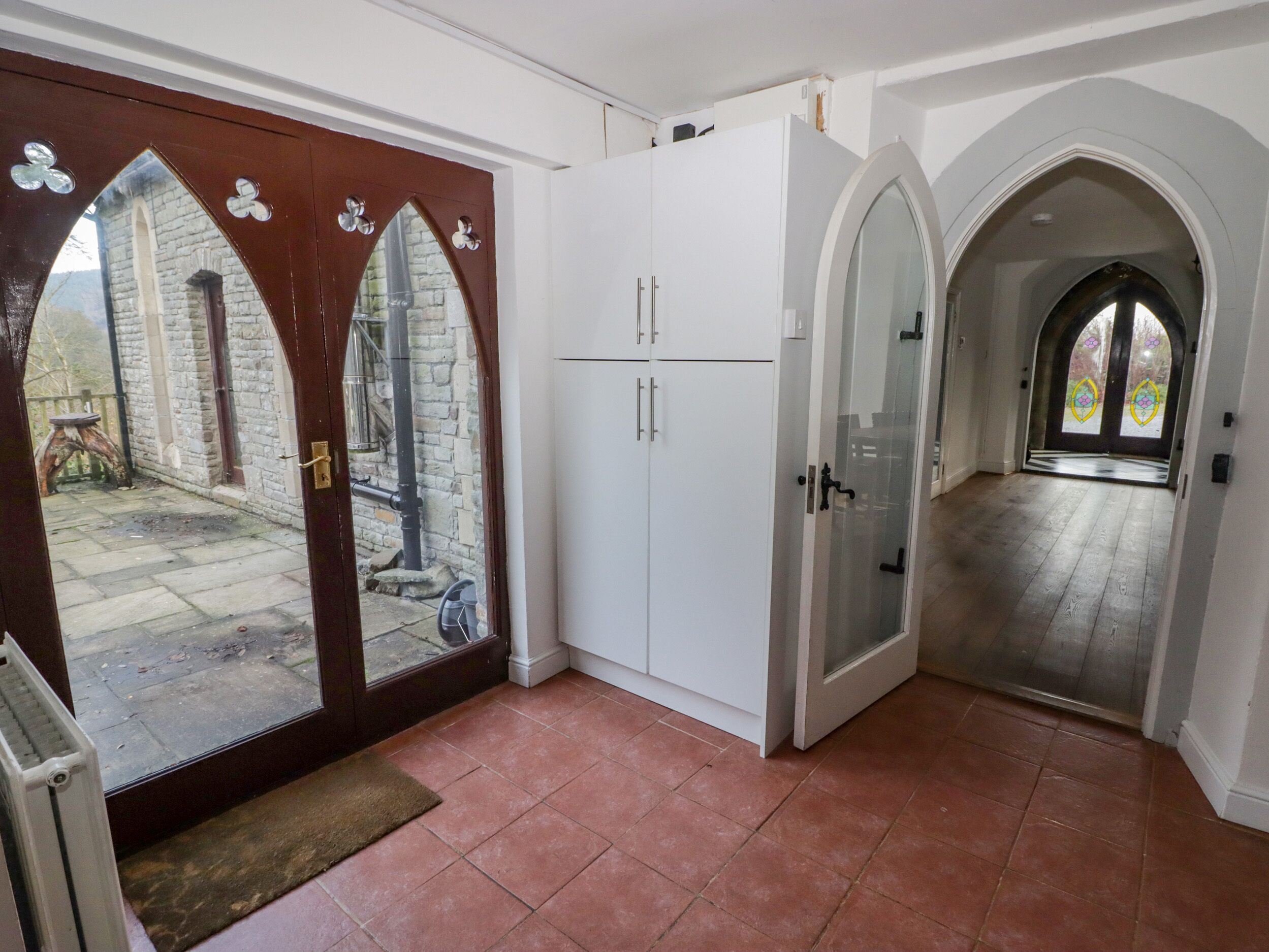 Un pasillo amplio con una puerta de madera grande que da a un patio interior, armarios blancos y vista a un edificio de piedra.