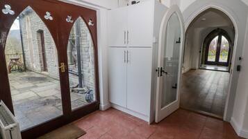 Un pasillo amplio con una puerta de madera grande que da a un patio interior, armarios blancos y vista a un edificio de piedra.