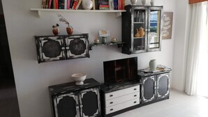 A living room with a TV, a bookshelf, and a cabinet with decorative items. - Les Motes 7º, Solo Familias ! (Xeraco Playa)