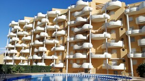 A multi-story hotel with balconies, a swimming pool, and a clear blue sky. - Les Motes 7º, Solo Familias ! (Xeraco Playa)