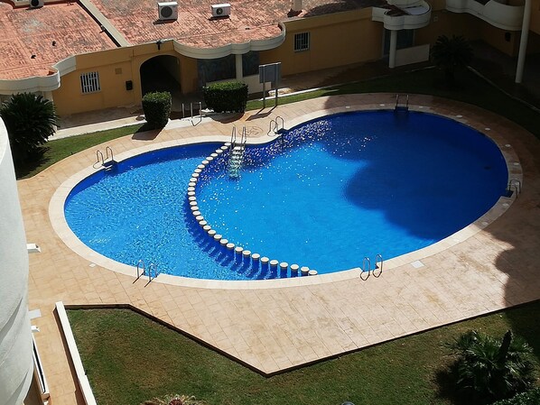 Une piscine circulaire à eau cristalline, dont le centre est d’un bleu éclatant, entourée d’une terrasse carrelée et d’une petite pelouse.