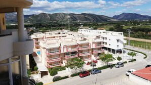 A multi-story residential building with balconies, a street in front, and mountains in the background. - Les Motes 7º, Solo Familias ! (Xeraco Playa)