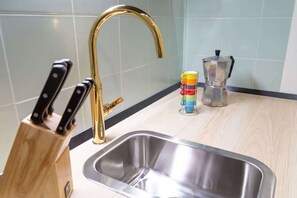 A kitchen with a stainless steel sink, a gold faucet, a coffee maker, and a knife block. - Lovely and tiny Pied-à-terre in the City center (Trieste)
