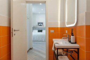 Une salle de bain avec un mur recouvert de carreaux orange, un lavabo blanc et un miroir.