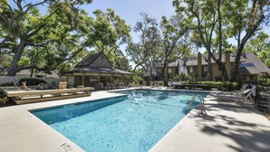 Une piscine rectangulaire avec un escalier, entourée de chaises longues et d’un espace ombragé.
