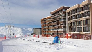 A modern hotel with multiple balconies, a ski lift in the background, and a snowy landscape.