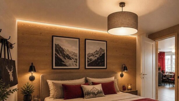 A bedroom with a bed, two framed pictures, a hanging lamp, and a door leading to another room.