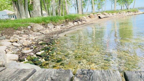 Una banchina di legno che si protende in un lago limpido, con una riva rocciosa e alberi sullo sfondo.