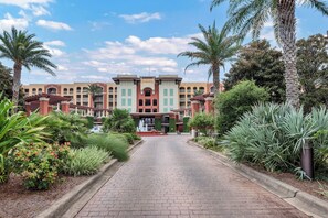 A hotel entrance with a brick pathway, palm trees, and a building with a central archway. - Azure 222/Great Pools/Gorgeous Beach/Beach Service/Resort Renovated 2025 (Fort Walton Beach)