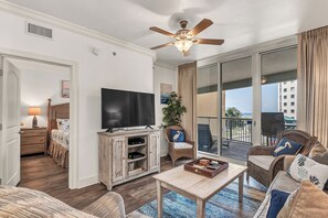 A living room with a ceiling fan, a TV, a wooden cabinet, a sofa, a chair, and a balcony with a view.