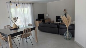 A dining area with a table and chairs, a sofa, a TV, and a vase with pampas grass.