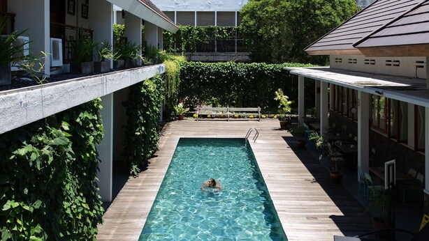 A rectangular swimming pool with clear water, surrounded by wooden deck and greenery, with buildings on either side. - Blambangan Hotel (Banyuwangi)