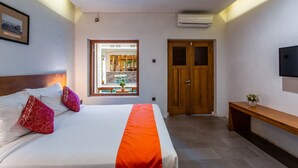A hotel room with a bed, a wooden door, a bench, and a TV. - Blambangan Hotel (Banyuwangi)