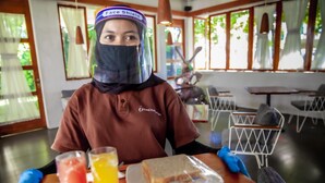 A person seated at a table with a sandwich and drinks, wearing a face shield. - Blambangan Hotel (Banyuwangi)