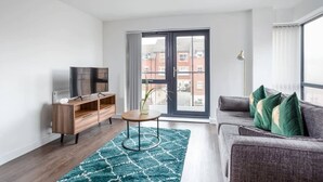 Una sala de estar moderna con un sofá, un televisor, un mueble de madera y un ventanal con vistas a edificios.
