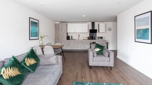 Una sala de estar moderna con un sofá y sillones grises, una mesa de comedor y una cocina al fondo.