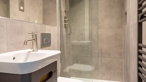 Un baño moderno con lavamanos, inodoro y cabina de ducha con mampara de vidrio.