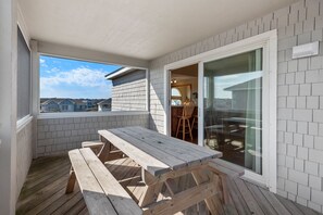 Un patio techado con mesa y bancos de madera, un ventanal corredero y vistas a casas vecinas.