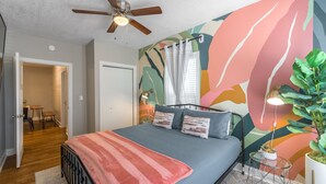 Un dormitorio con cama, ventilador de techo, mural en la pared y planta en maceta.