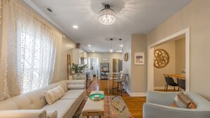 Una sala de estar moderna con sofá, sillón y mesa de centro. Se ve una cocina al fondo con zona de comedor.
