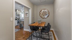 Un comedor con una mesa de madera y sillas negras, un adorno en la pared y vista a la cocina.