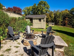 A backyard with Adirondack chairs, a stone fire pit, and a wooden shed. - Renovated Downtown Great Barrington House (Great Barrington)