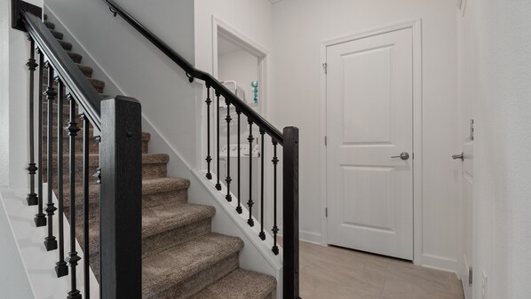 Un escalier avec une rampe noire, des marches recouvertes de moquette et une porte blanche en haut.