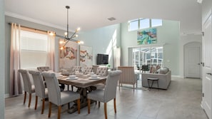 Une salle à manger spacieuse, agrémentée d’un lustre moderne, d’une grande table dressée pour six personnes et d’un mobilier confortable.