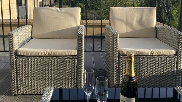 En balkon med fletmøbler, to vinglas og en champagneflaske.
