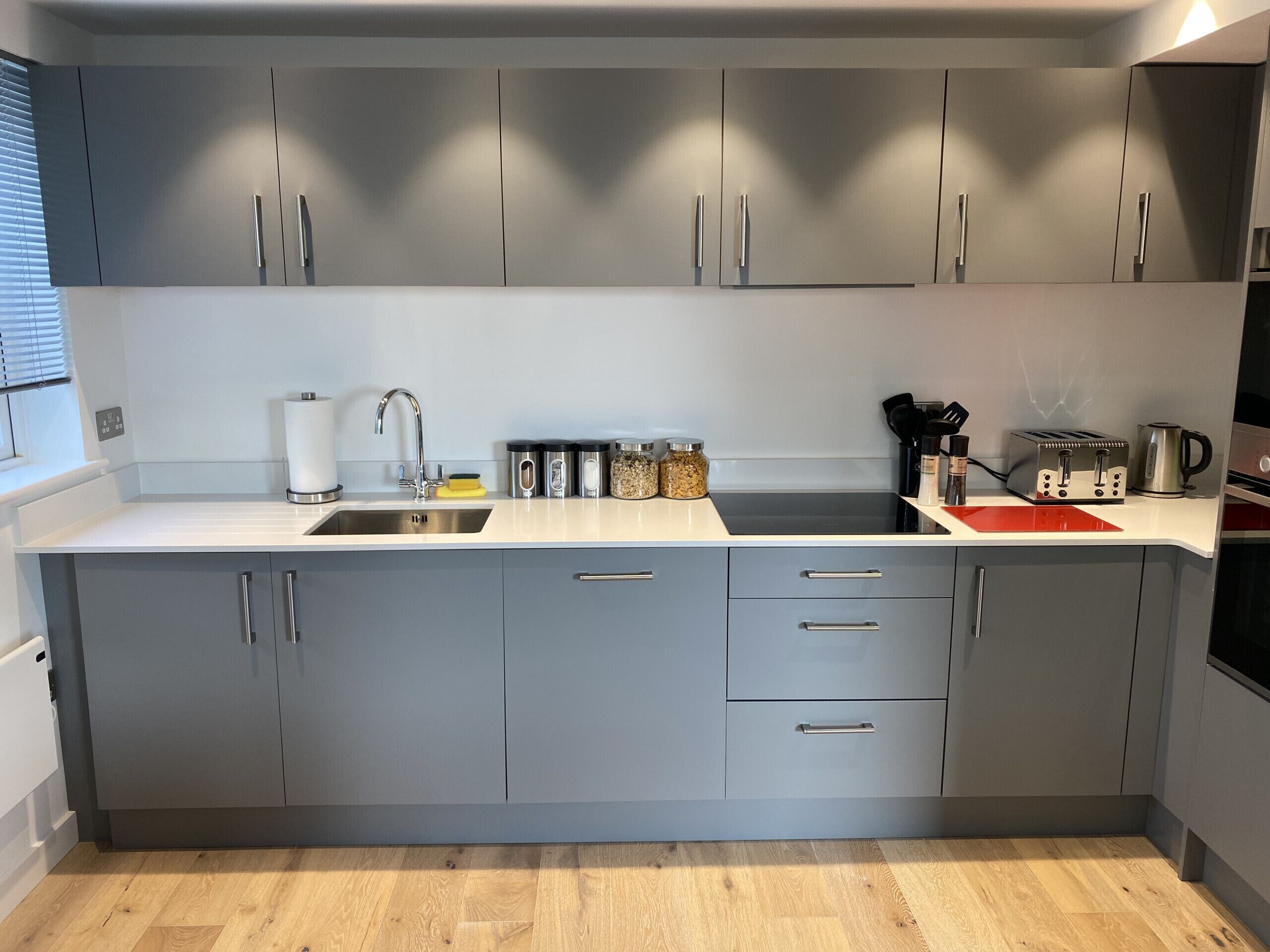Une cuisine moderne avec des meubles gris, un évier en acier inoxydable et un grille-pain noir.