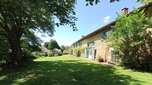 A stone house with a well-maintained lawn and a large tree in the foreground. - Bed and breakfast - Le Bonheur du Périgord (Miallet)